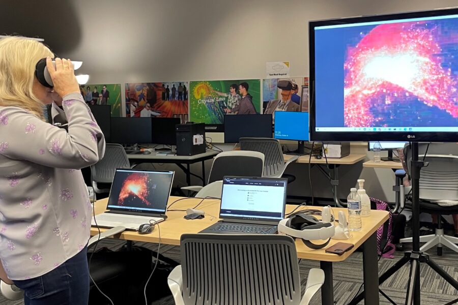 Visitor participates in hands-on experiences of AR & VR projects in the visualization lab. Participant is standing while holding VR goggles. The TV features what the visitor is seeing in the goggles.