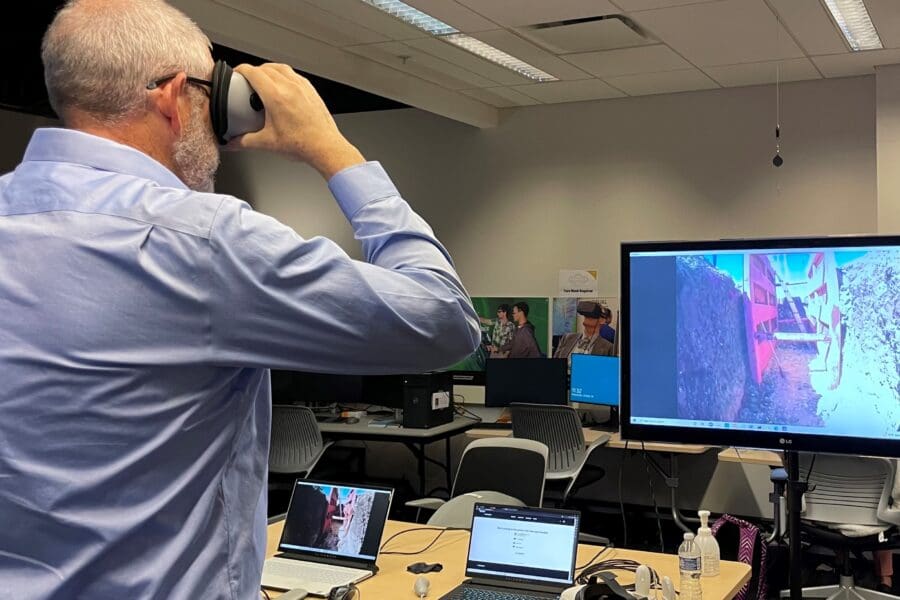 Visitor participates in hands-on experiences of AR & VR projects in the visualization lab. Participant is standing while holding VR goggles. The TV features what the visitor is seeing in the goggles.