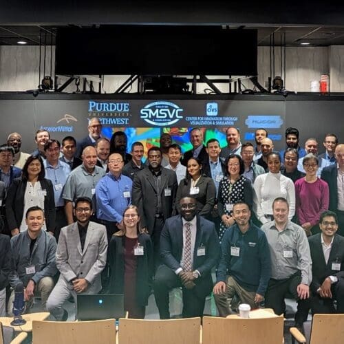 A large group of individuals in business professional attire stand together in front of a large screen.