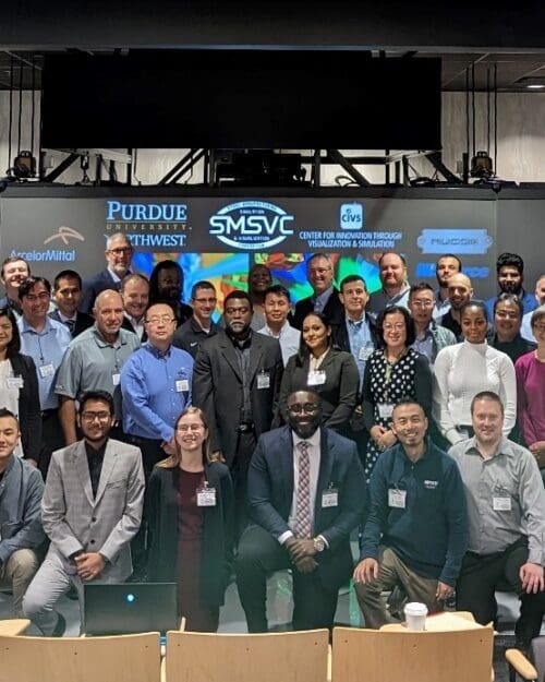 A large group of individuals in business professional attire stand together in front of a large screen.