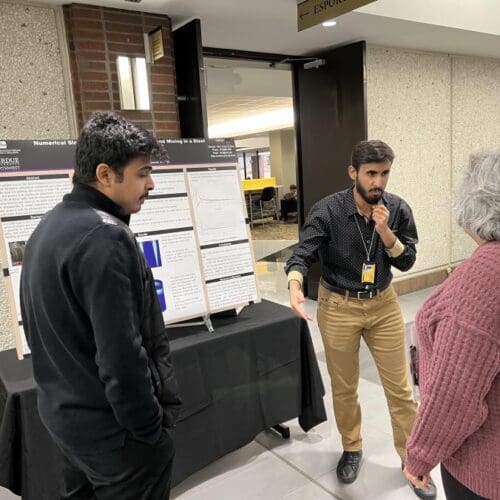 Students standing and talking to faculty member in front of academic poster in hallway