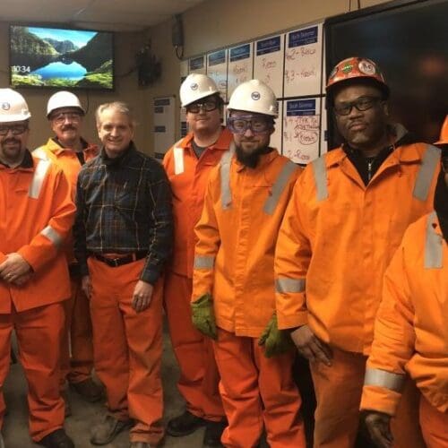 Individuals in conference room wearing bright orange uniform jumpsuits and white hard hats