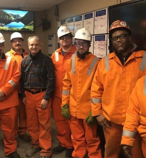 Individuals in conference room wearing bright orange uniform jumpsuits and white hard hats