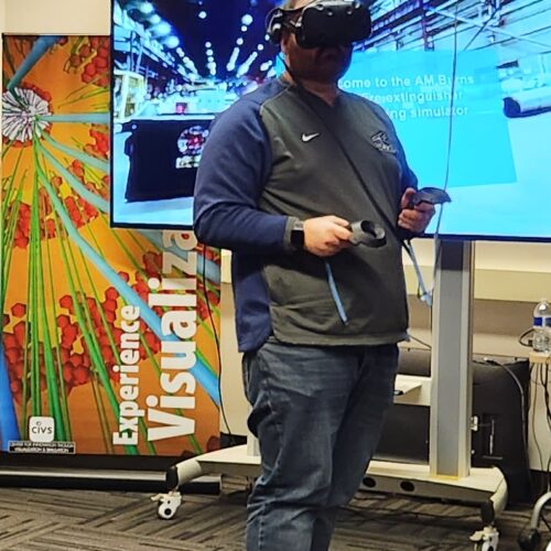 Visitor participates in hands-on experiences of AR & VR projects in the visualization lab. Participant is standing while wearing a tethered VR headset and manipulating hand held controllers