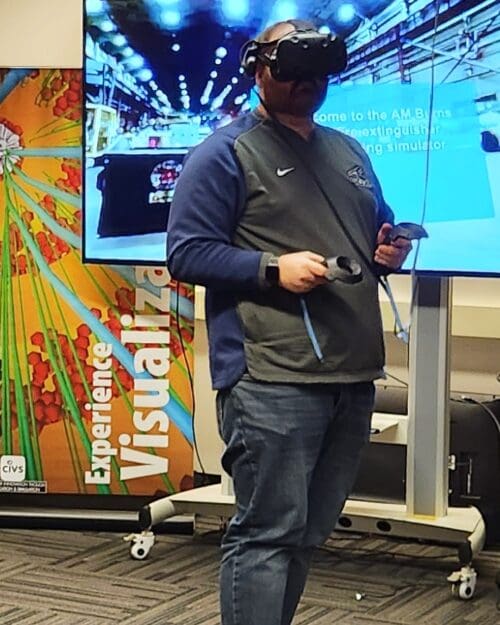 Visitor participates in hands-on experiences of AR & VR projects in the visualization lab. Participant is standing while wearing a tethered VR headset and manipulating hand held controllers