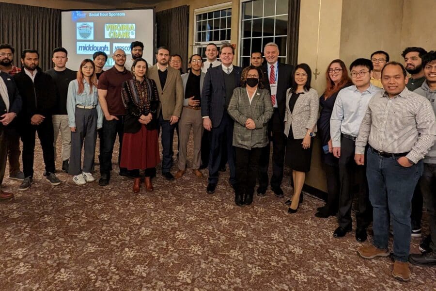 A large group of individuals in business professional attire stand together in front of a large screen.