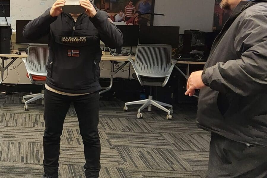 Visitor participates in hands-on experiences of AR & VR projects in the visualization lab. Participant is standing while holding VR goggles. Another individual gives instruction.