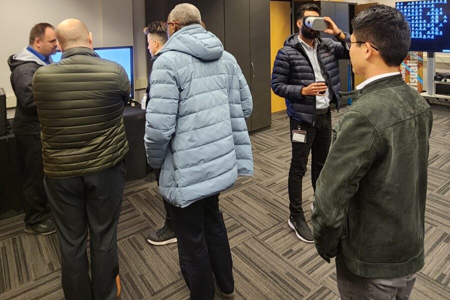 Visitor participates in hands-on experiences of AR & VR projects in the visualization lab. Participant is standing while holding VR goggles surrounded by several people observing