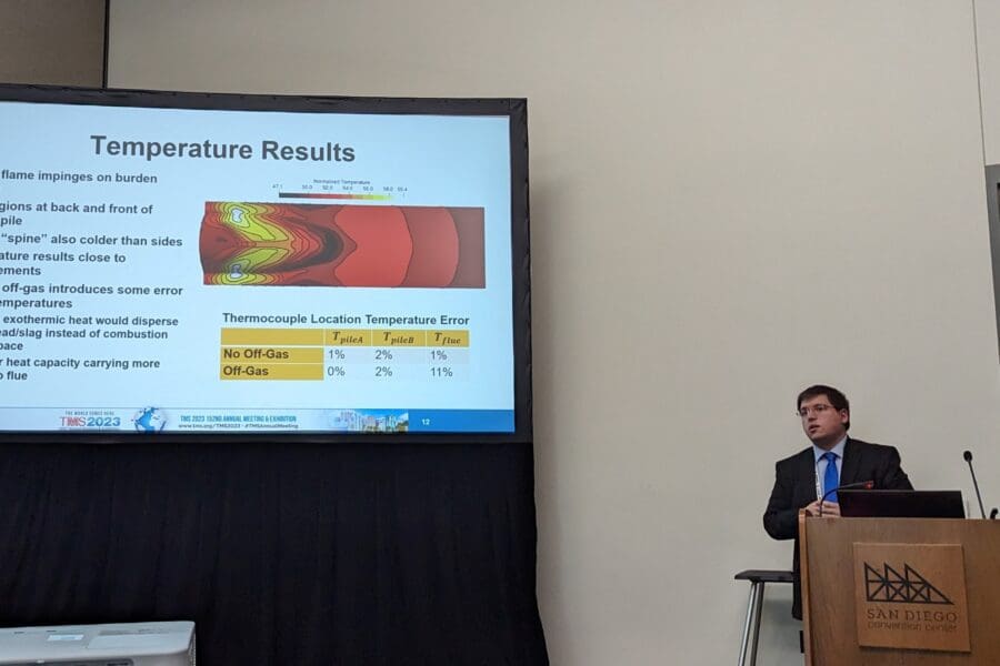 Man standing in front of screen featuring PowerPoint slide at podium in conference room