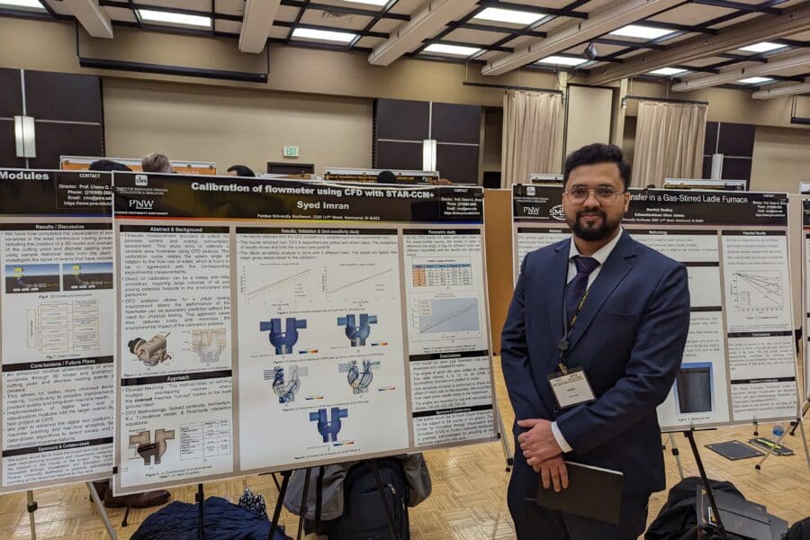 Student in a professional business attire standing in front of academic poster in presentation hall