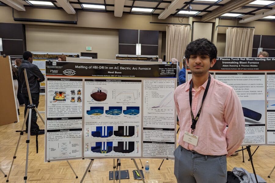 Student in a professional business attire standing in front of academic poster in presentation hall