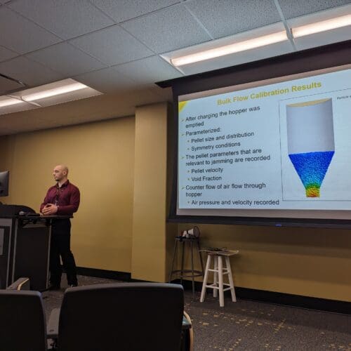 Man standing in front of screen featuring PowerPoint slide at podium in conference room