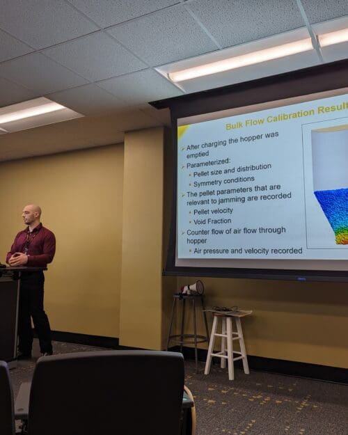 Man standing in front of screen featuring PowerPoint slide at podium in conference room