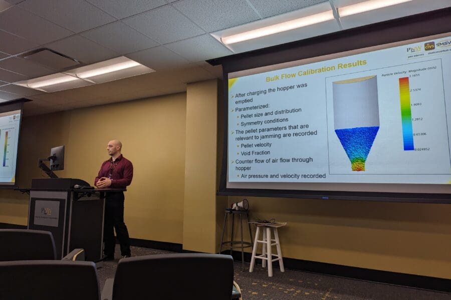 Man standing in front of screen featuring PowerPoint slide at podium in conference room