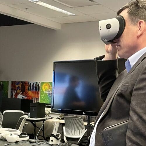 Visitor participates in hands-on experiences of AR & VR projects in the visualization lab. Participant is standing while holding VR goggles.