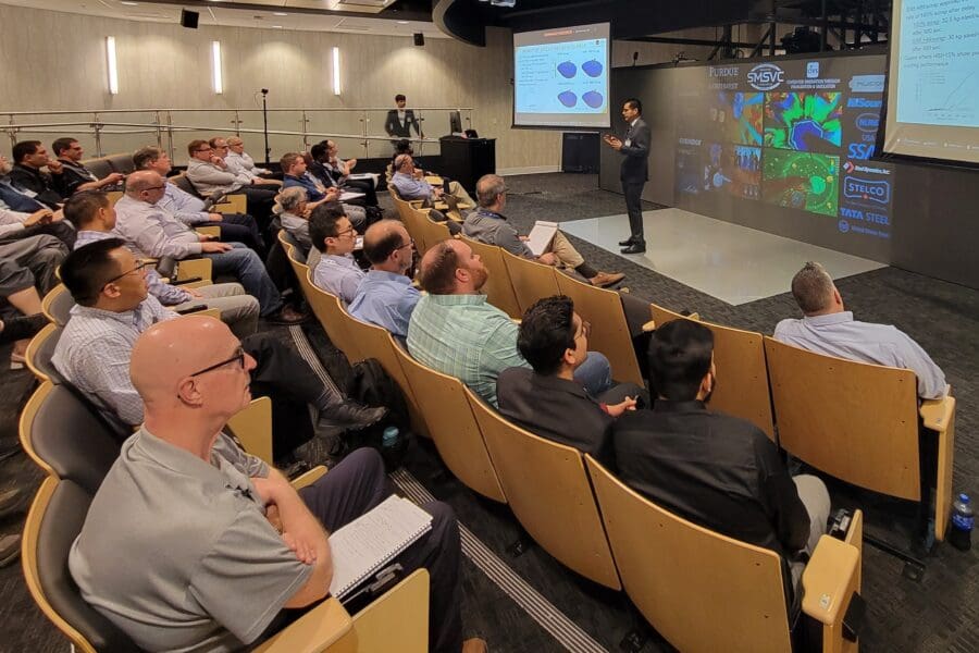 Man standing in front of screen in auditorium with several people seated in rows of chairs