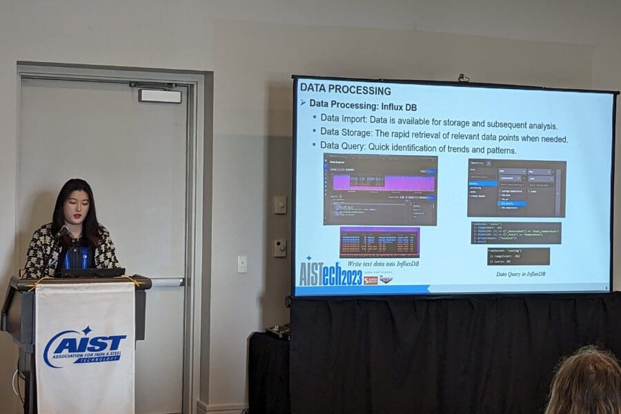 Woman standing and talking in front of screen featuring PowerPoint slide at podium in conference room