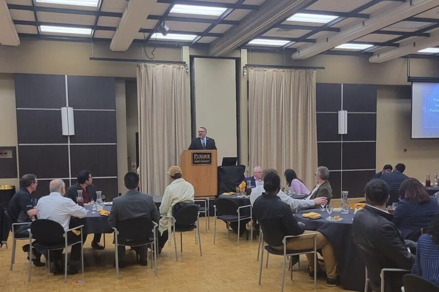 Man standing at podium in front of guests seated at several round tables