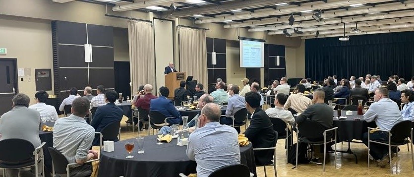 Man standing at podium in front of guests seated at several round tables