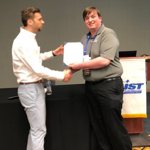 Man in business casual attire handing certificate to program participant and shaking their hand
