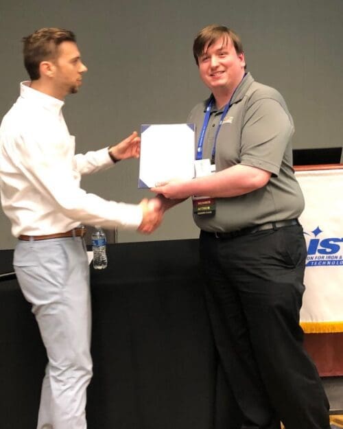 Man in business casual attire handing certificate to program participant and shaking their hand