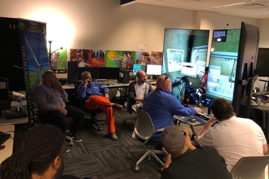 An individual operates a crane training simulator in the CIVS visualization lab while other individuals watch