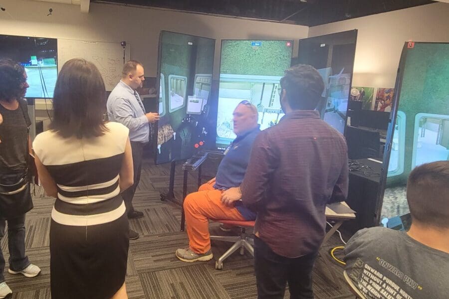 An individual in business professional attire operates a crane training simulator in the CIVS visualization lab while other individuals watch