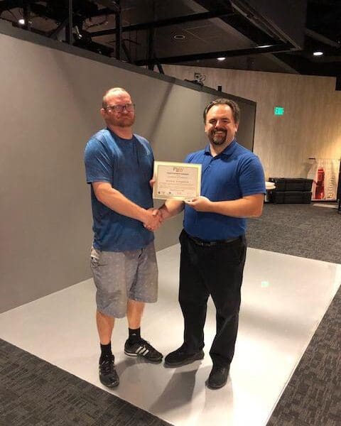 Man in business attire handing certificate to program participant and shaking their hand