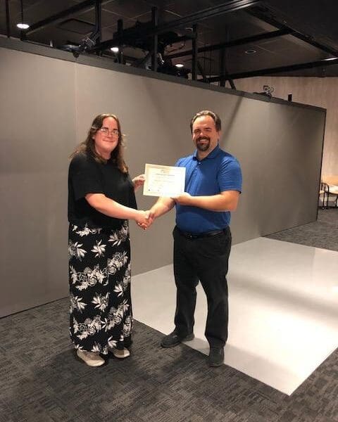 Man in business attire handing certificate to program participant and shaking their hand