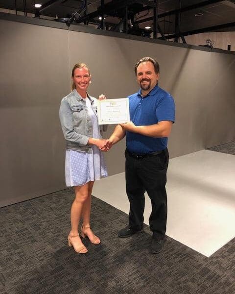 Man in business attire handing certificate to program participant and shaking their hand