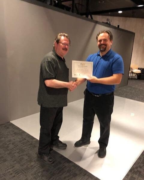 Man in business attire handing certificate to program participant and shaking their hand