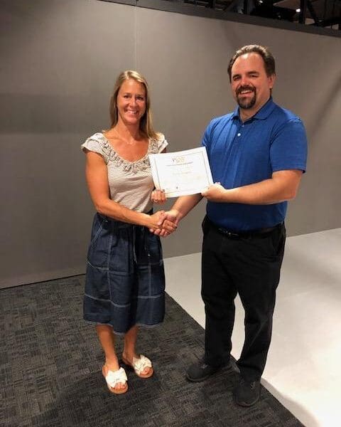 Man in business attire handing certificate to program participant and shaking their hand