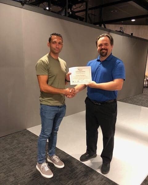 Man in business attire handing certificate to program participant and shaking their hand