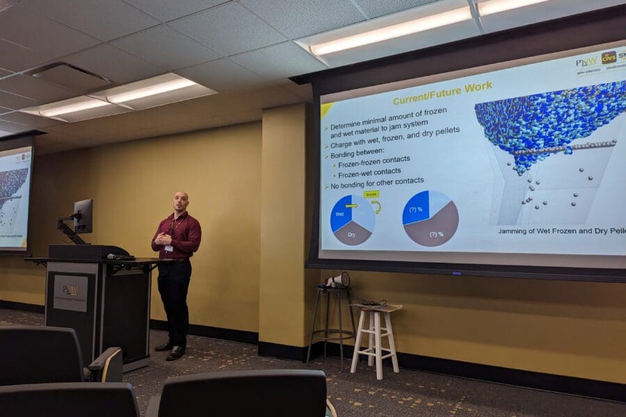 Man standing in front of screen featuring PowerPoint slide at podium in conference room