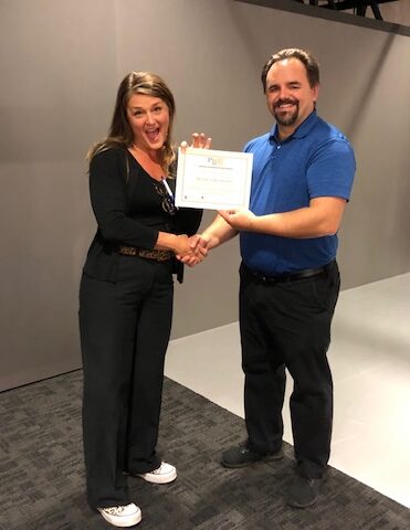 Man in business attire handing certificate to program participant and shaking their hand