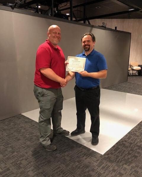 Man in business attire handing certificate to program participant and shaking their hand