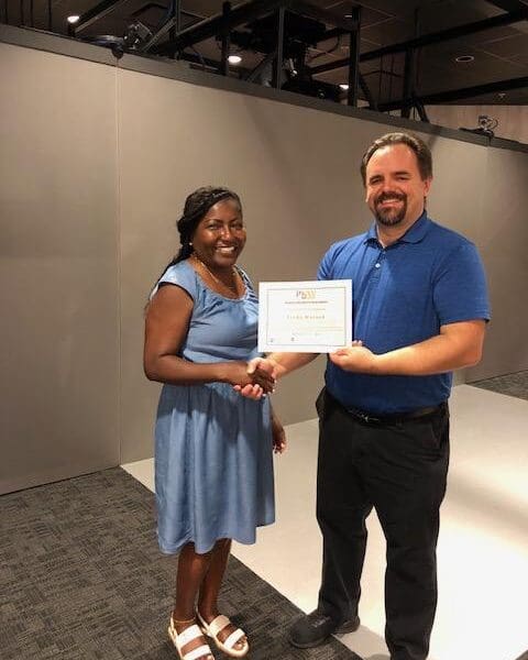 Man in business attire handing certificate to program participant and shaking their hand