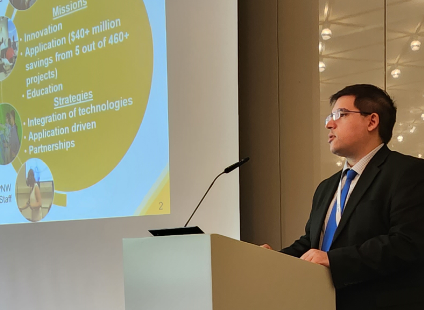 Man standing in front of screen featuring PowerPoint slide at podium in conference room