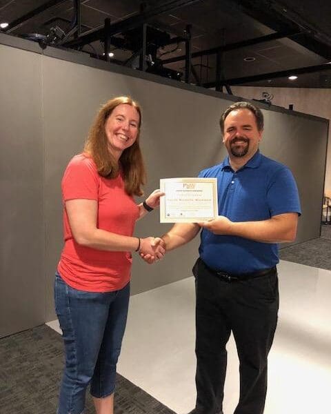 Man in business attire handing certificate to program participant and shaking their hand