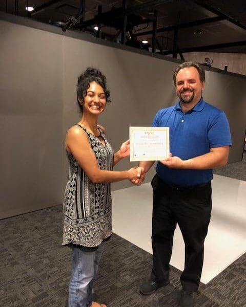 Man in business attire handing certificate to program participant and shaking their hand