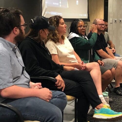 Several people seated in a row at the front of a conference room, a lady speaks while the others face her