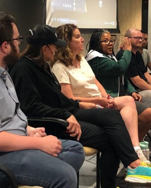 Several people seated in a row at the front of a conference room, a lady speaks while the others face her