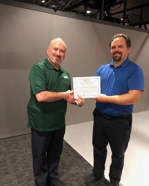 Man in business attire handing certificate to program participant and shaking their hand