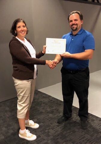 Man in business attire handing certificate to program participant and shaking their hand