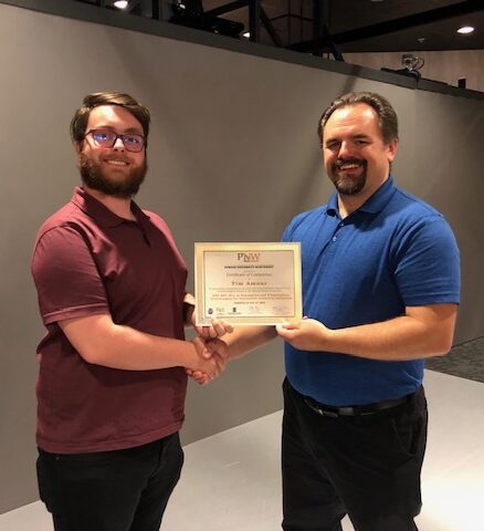 Man in business attire handing certificate to program participant and shaking their hand