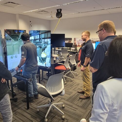 An individual operates a crane training simulator in the CIVS visualization lab while other individuals watch