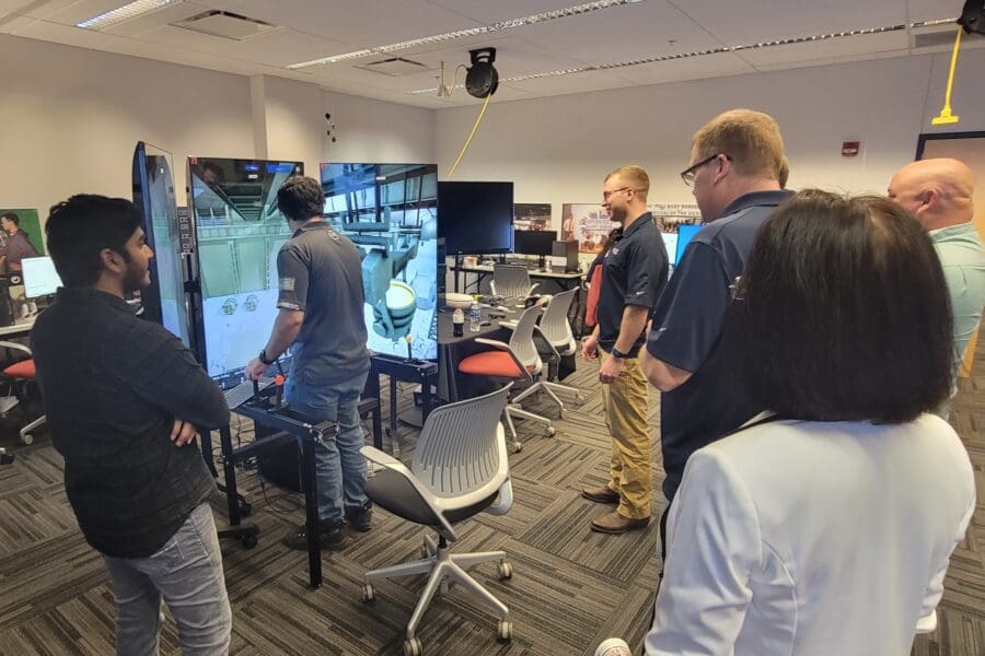 An individual operates a crane training simulator in the CIVS visualization lab while other individuals watch