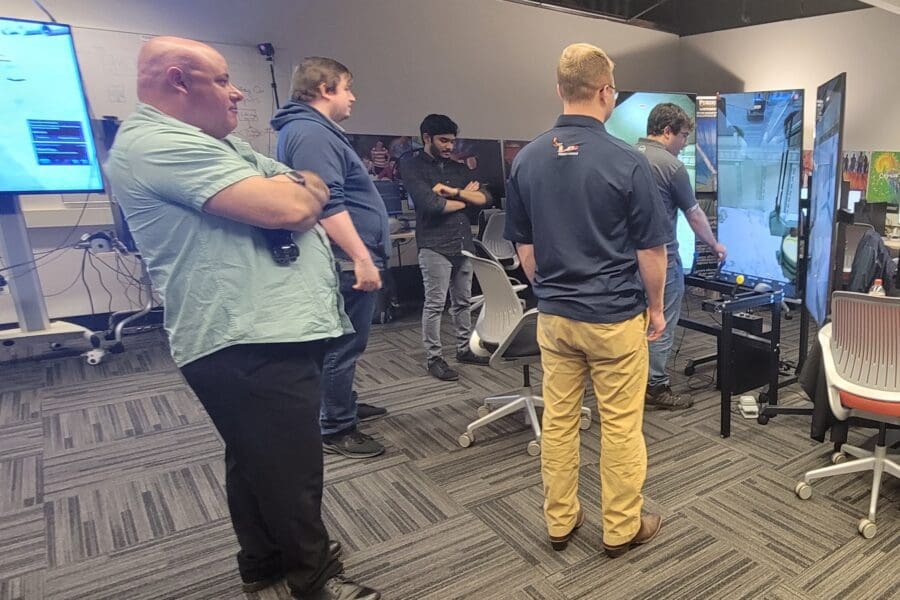 An individual operates a crane training simulator in the CIVS visualization lab while other individuals watch