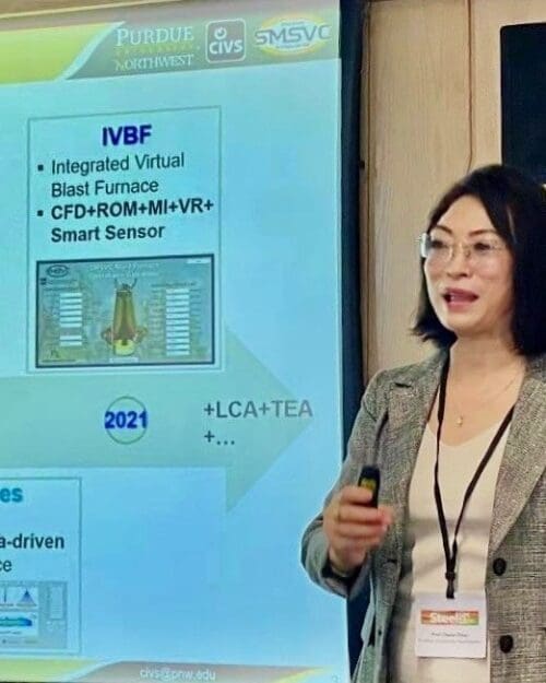 Chenn Zhou standing and speaking in front of screen featuring PowerPoint slide titled Journey to Smart Manufacturing in conference room