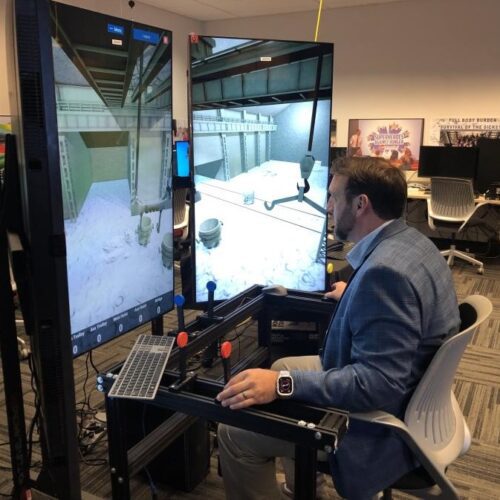 An individual in business professional attire operates a crane training simulator in the CIVS visualization lab